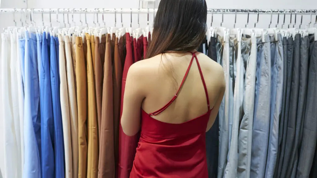 Joven mujer de espaldas analiza un perchero que muestra pantalones de varios colores
