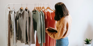 Joven mujer especialista en moda analiza un vestuario colgado de un perchero.