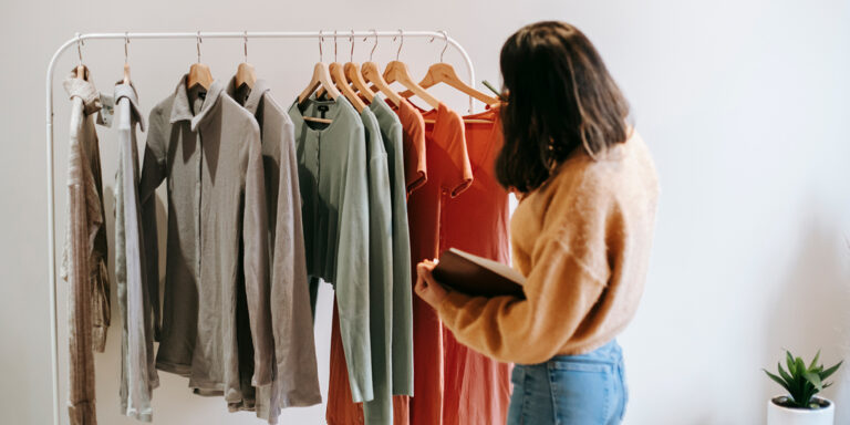 Joven mujer especialista en moda analiza un vestuario colgado de un perchero.